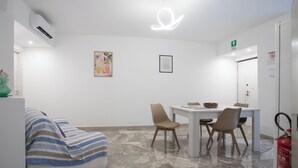 Moderni hotellihuone, jossa on sänky, ruokapöytä tuoleineen, sammutin ja kattovalaisin.