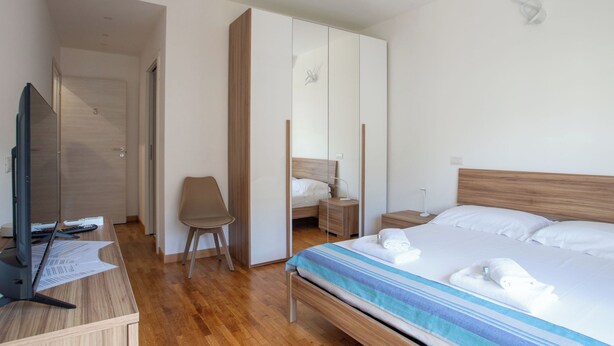 Hotellihuone, jossa on puinen sänky, työpöytä tietokoneella, tuoli, vaatekaappi ja yöpöytä, jossa on lamppu.
