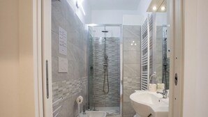 Moderni kylpyhuone, jossa on lasiseinällä varustettu suihku, valkoinen pesuallas ja wc.