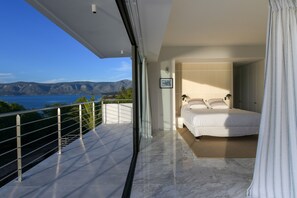 Ein Schlafzimmer mit einem großen Bett, Meerblick und einem Balkon mit Geländer.