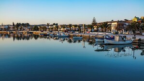 A marina with boats docked, calm water, and buildings in the background. - Kilada on the Rocks (Doroufi Kranidiou)