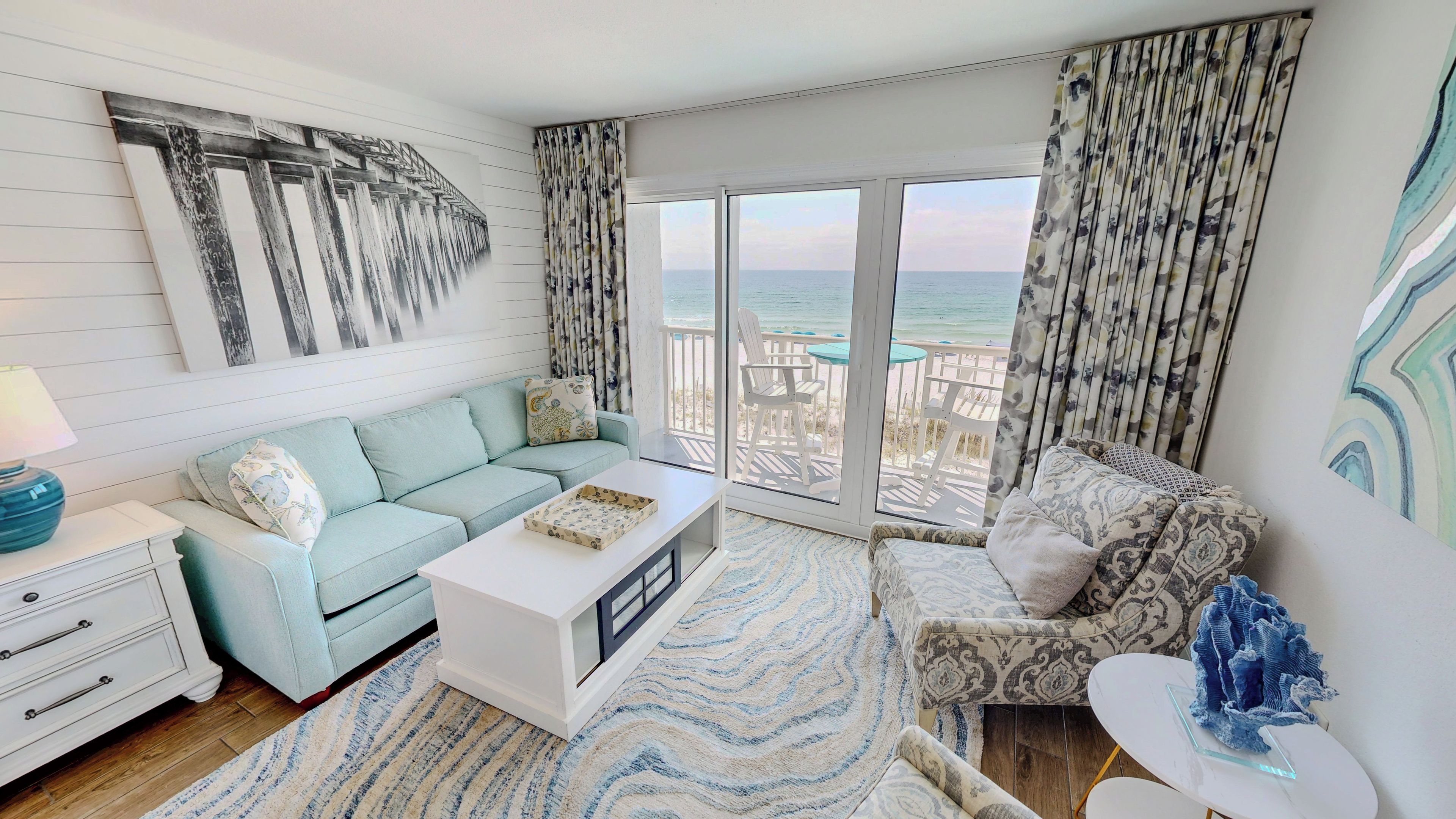 Un salon moderne avec un canapé, une table basse et une vue sur la plage grâce à de grandes fenêtres.