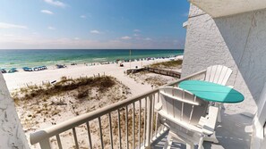 Ein Balkon mit Blick auf einen Strand, ein weißer Stuhl und ein kleiner Tisch.
