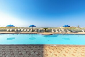 A swimming pool with lounge chairs and umbrellas, surrounded by a fence and a clear sky. - IBR 403 Stunning Beach Front Studio with Free Beach Service for 2 and W/D (Fort Walton Beach)