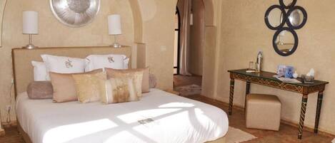 A bedroom with a large bed, two bedside lamps, a decorative mirror, and a small table with a chair.
