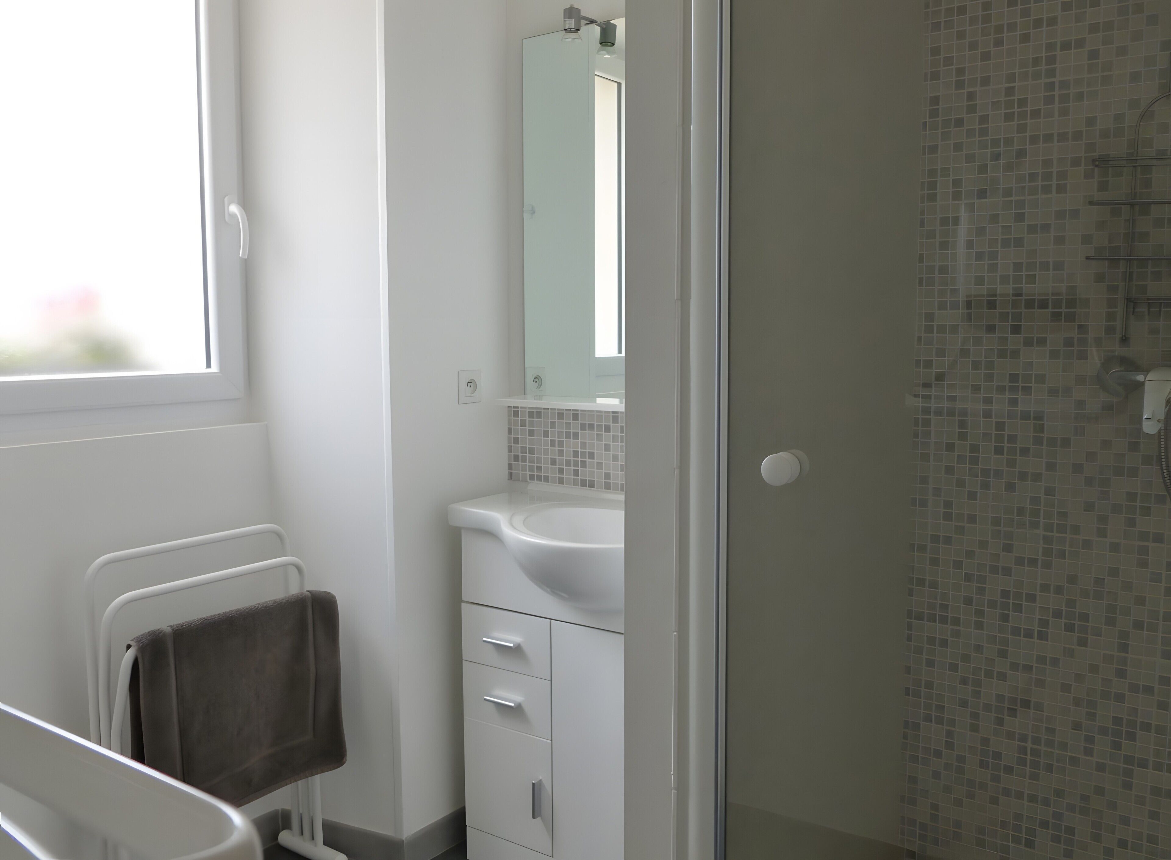 A bathroom with a shower, a sink, a mirror, and a towel rack.