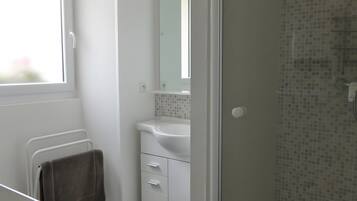 A bathroom with a shower, a sink, a mirror, and a towel rack.