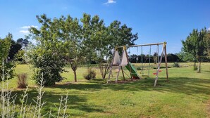Un parc amb gespa i un àrea de jocs que inclou cadiretes i tobogan.