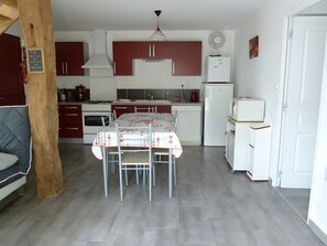 Une cuisine moderne avec une table à manger, des meubles rouges, des appareils électroménagers blancs et une structure en poutres apparentes.