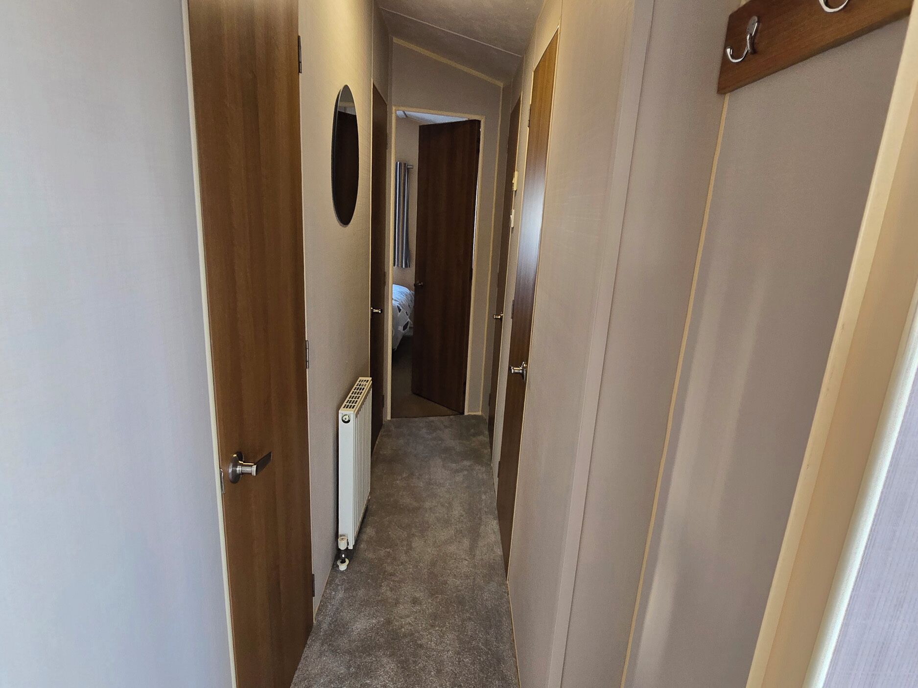 A narrow hallway with wooden doors, a radiator, and a carpeted floor.