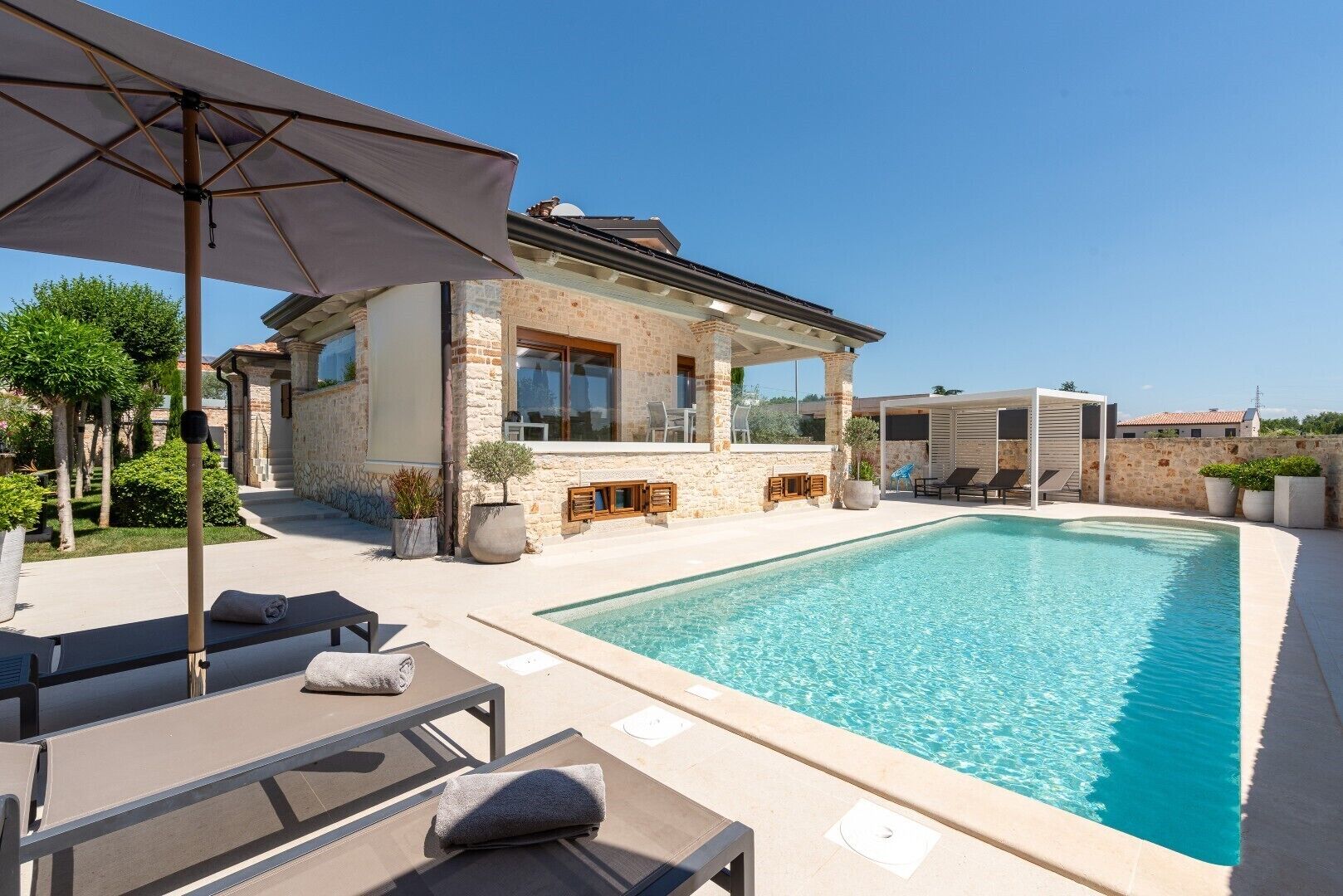 A poolside area with lounge chairs, a stone building, and a clear blue pool.