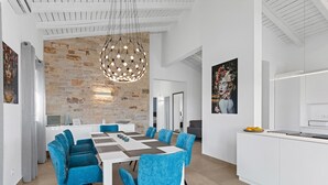 Una cocina moderna con muebles blancos, una isla central y un comedor con mantel a cuadros y sillas azules.