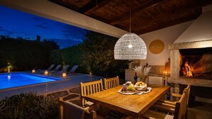 An outdoor dining area with a pool, wooden furniture, and a hanging light fixture. - Charming Villa Vin with pool near Poreč (Brčići)