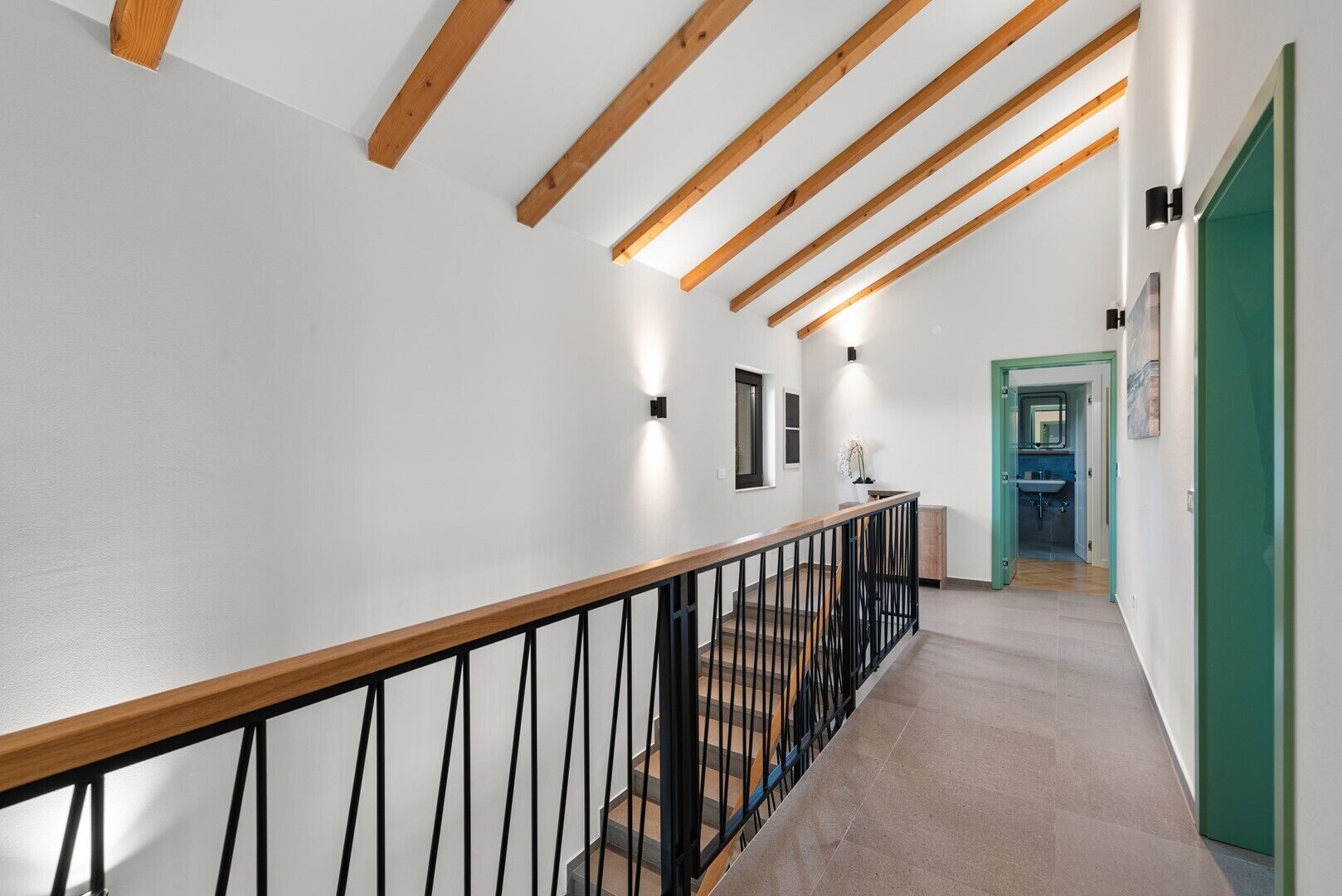 Un interior moderno con una escalera de madera, paredes blancas y una puerta verde que da acceso a un baño.