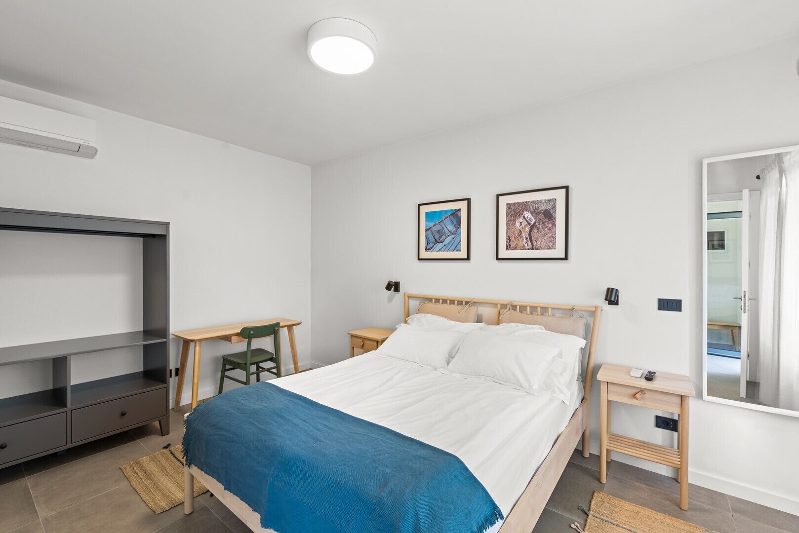 A bedroom with a bed, a desk, a chair, a TV, and two framed pictures on the wall.