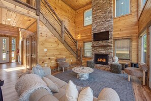 Un salón espacioso con chimenea de piedra, paredes de madera y una escalera.