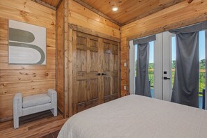 Una habitación con paneles de madera, una cama grande, un banco y una puerta que da a un espacio al aire libre.