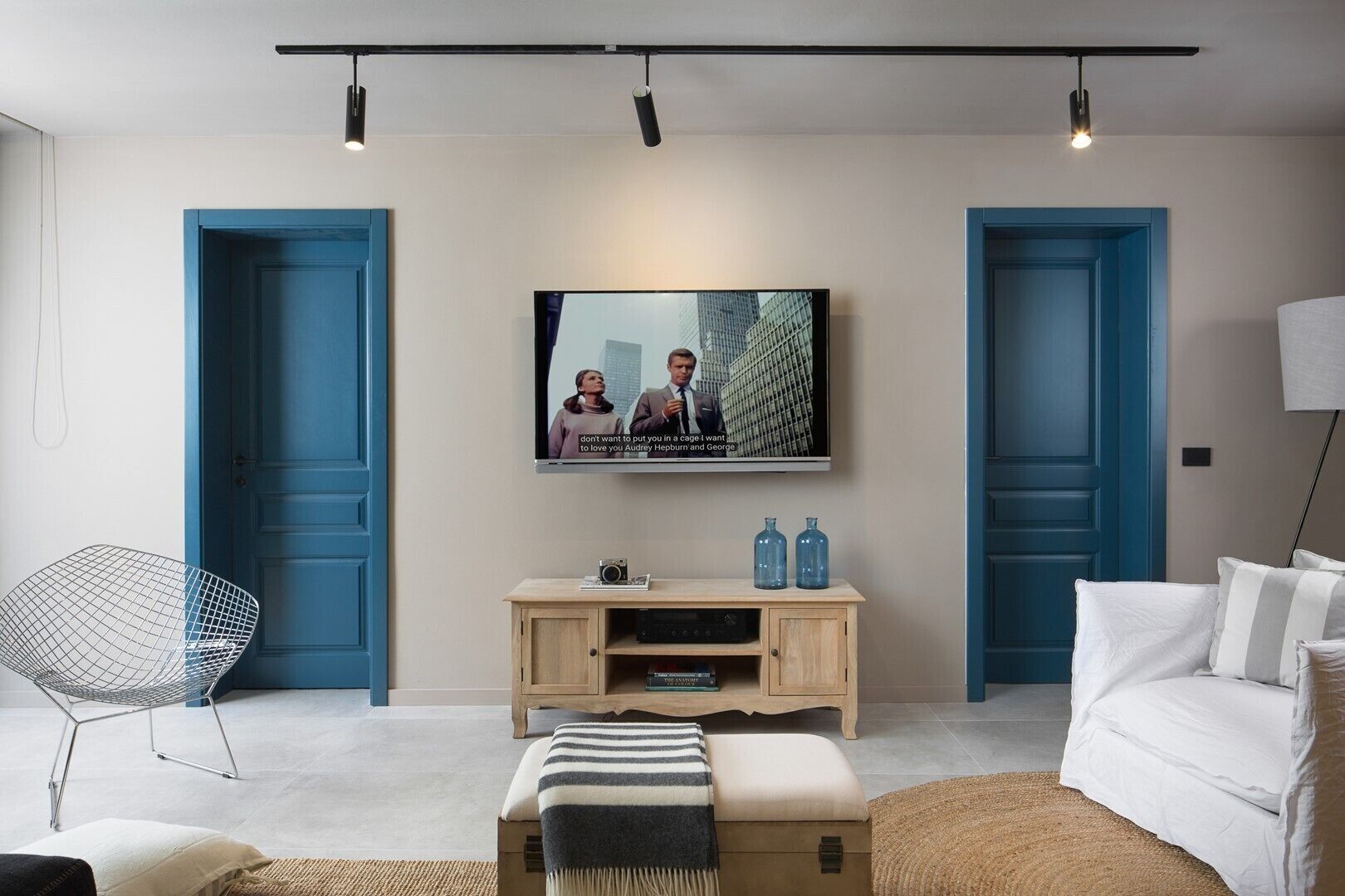 Un salon moderne avec un téléviseur à écran plat fixé au mur, un meuble en bois en dessous et un canapé blanc agrémenté de coussins à rayures.