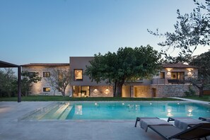 Una casa moderna de dos pisos con piscina, mobiliario exterior y muros de piedra.