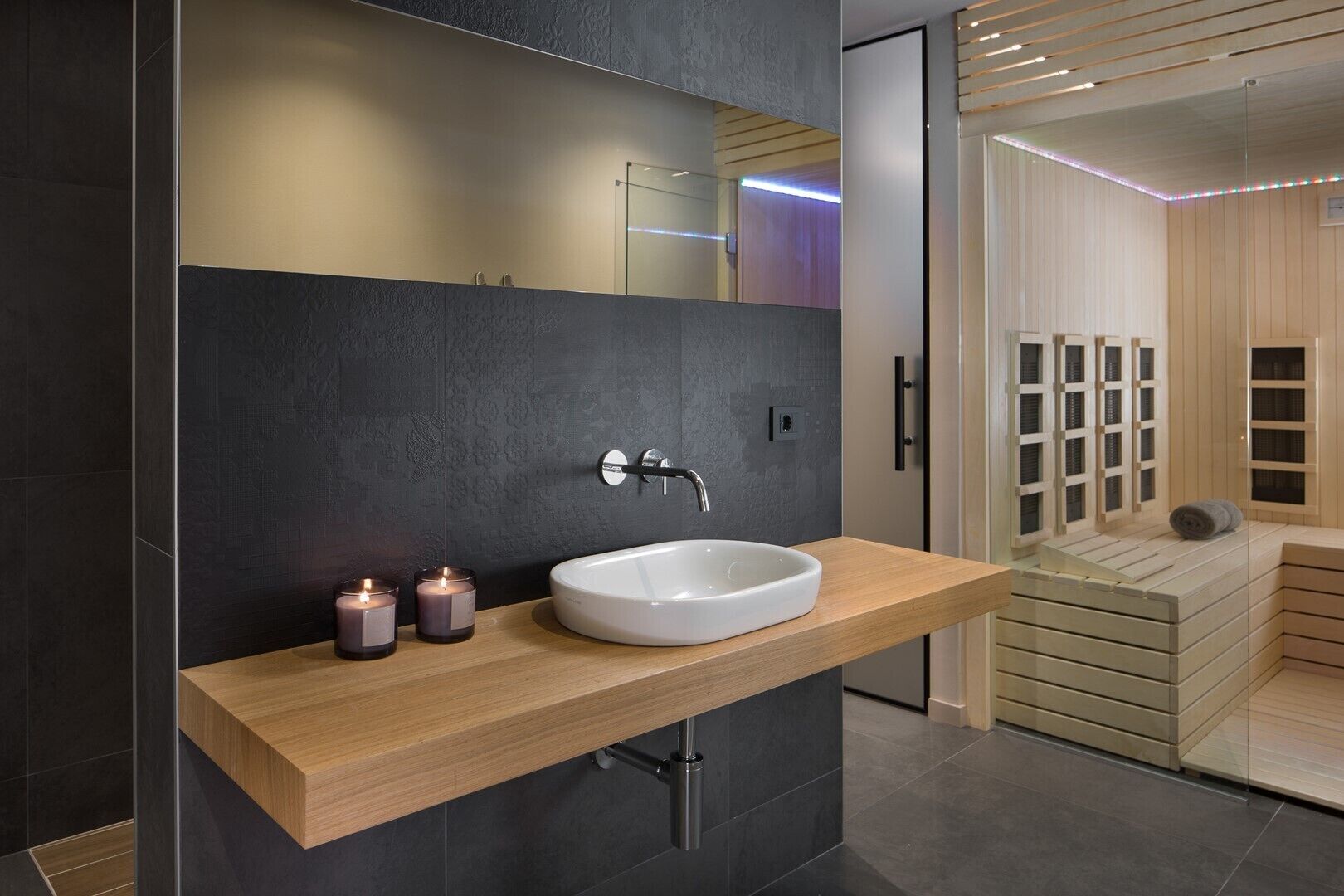 A modern bathroom with a large white sink, dark textured walls, and a wooden vanity.
