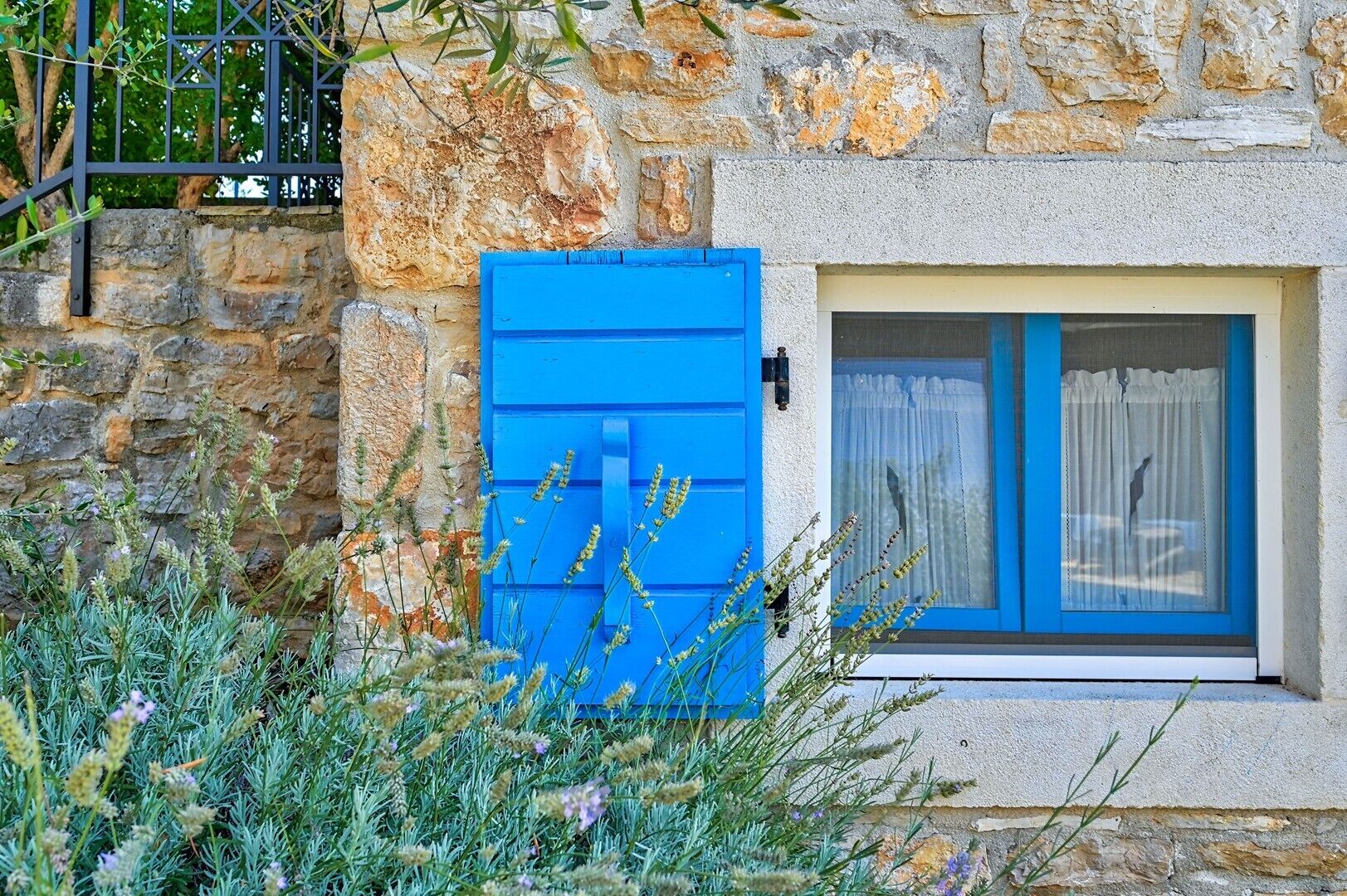 Ein Steinhaus mit einem blauen Fensterladen und einem Fenster mit weißen Vorhängen.