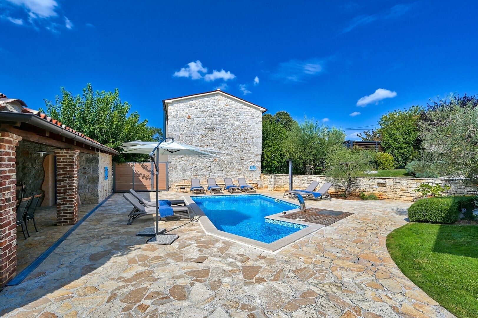Una piscina de pedra amb gandules, un edifici de pedra i un jardí ben cuidat.