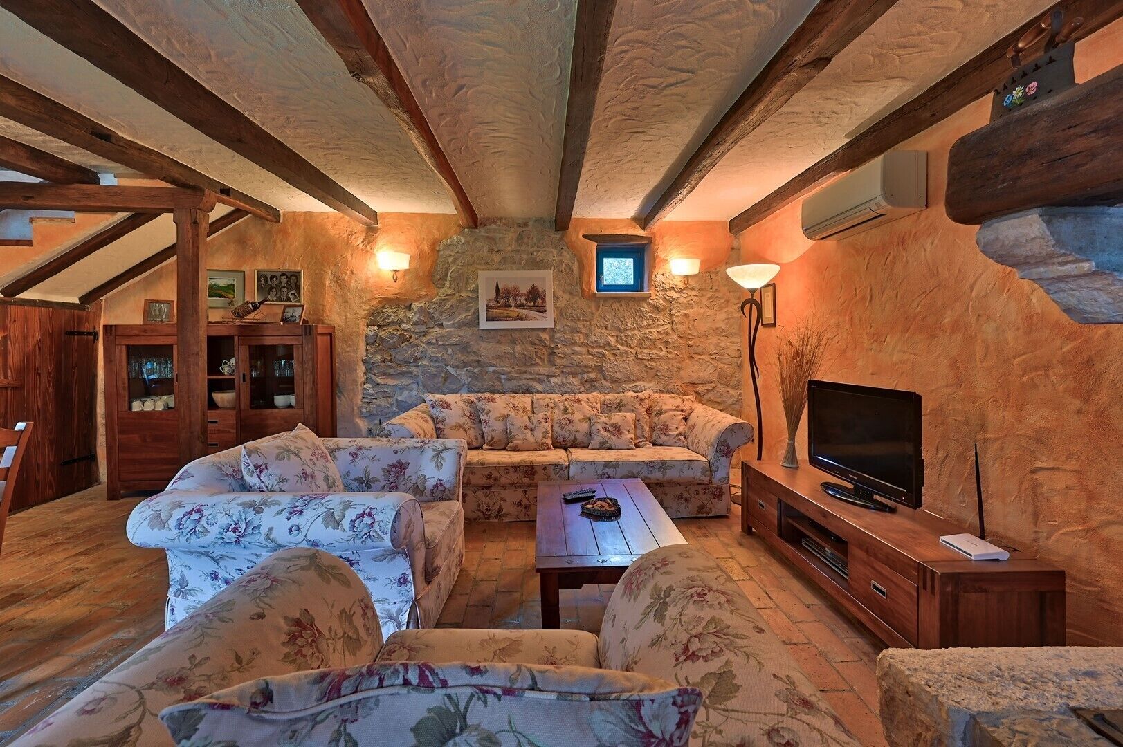 Un saló d'estar acollidor amb una paret de pedra, bigues de fusta, un sofà, una taula de café i una televisió.