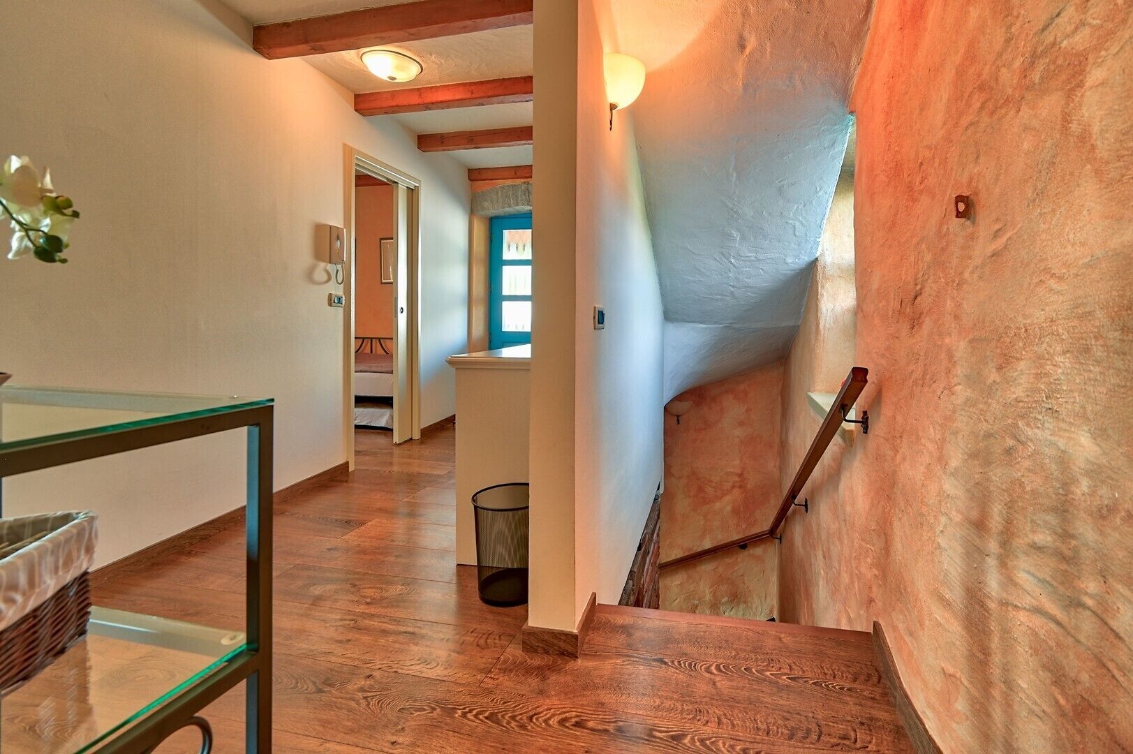 A staircase with wooden steps and a metal handrail, leading to a room with a white wall and a window.