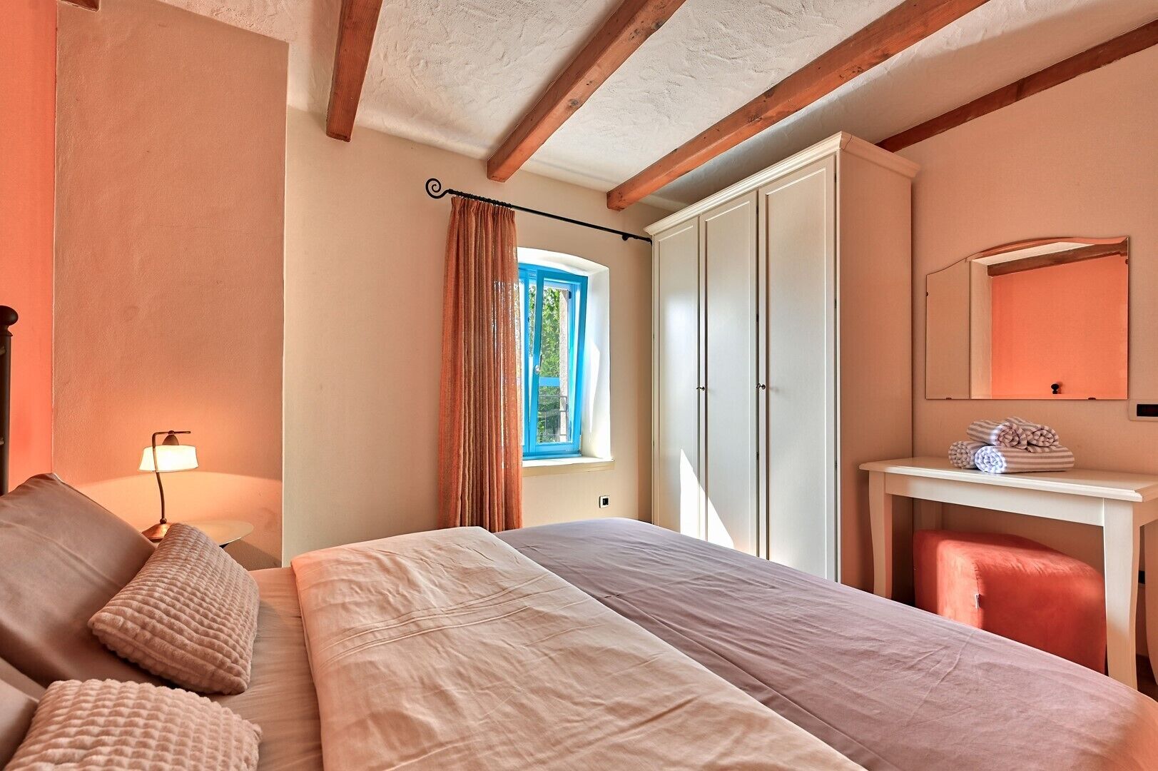 Ein Schlafzimmer mit Bett, Nachttisch, Lampe, Fenster und Kleiderschrank.
