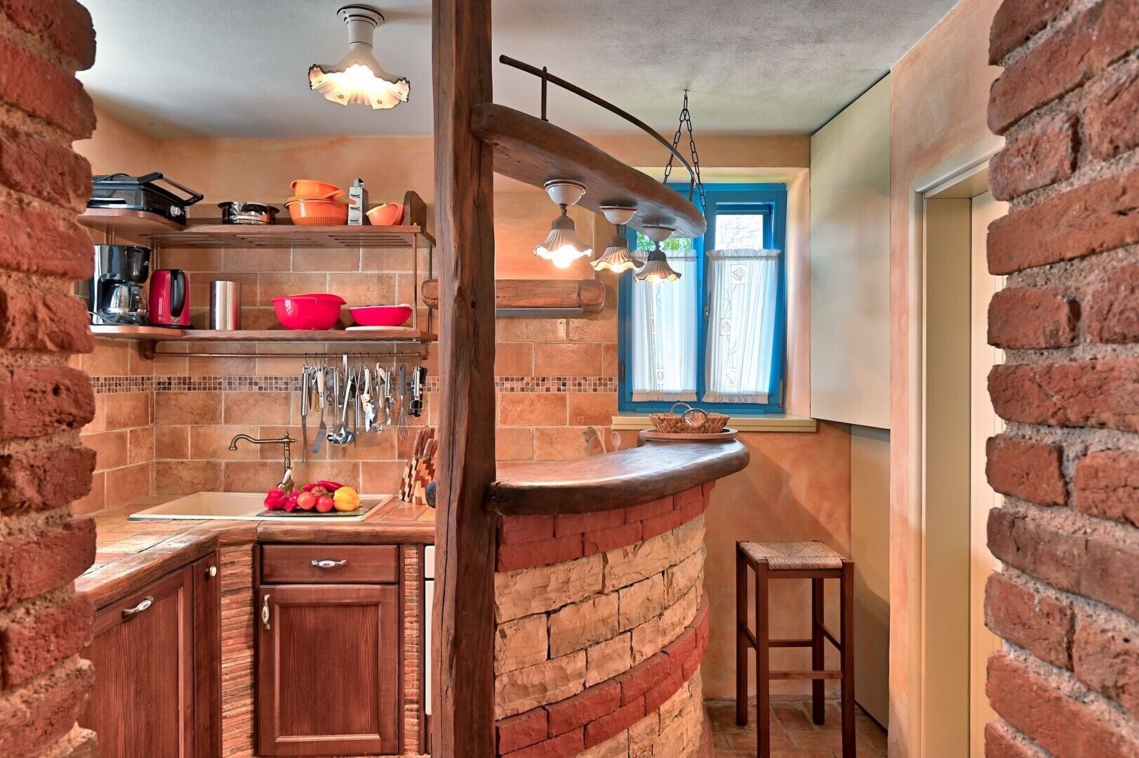 Een keuken met een bakstenen muur, houten keukenkastjes, een spoelbak en hangend keukengerei.