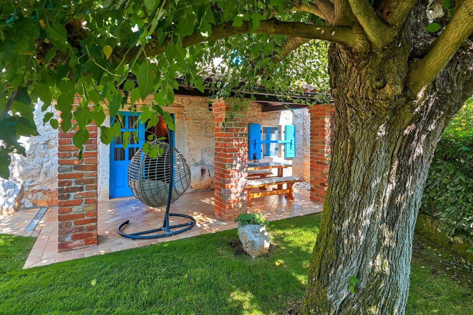 A rustic outdoor seating area with a brick wall, a hanging chair, and a table.