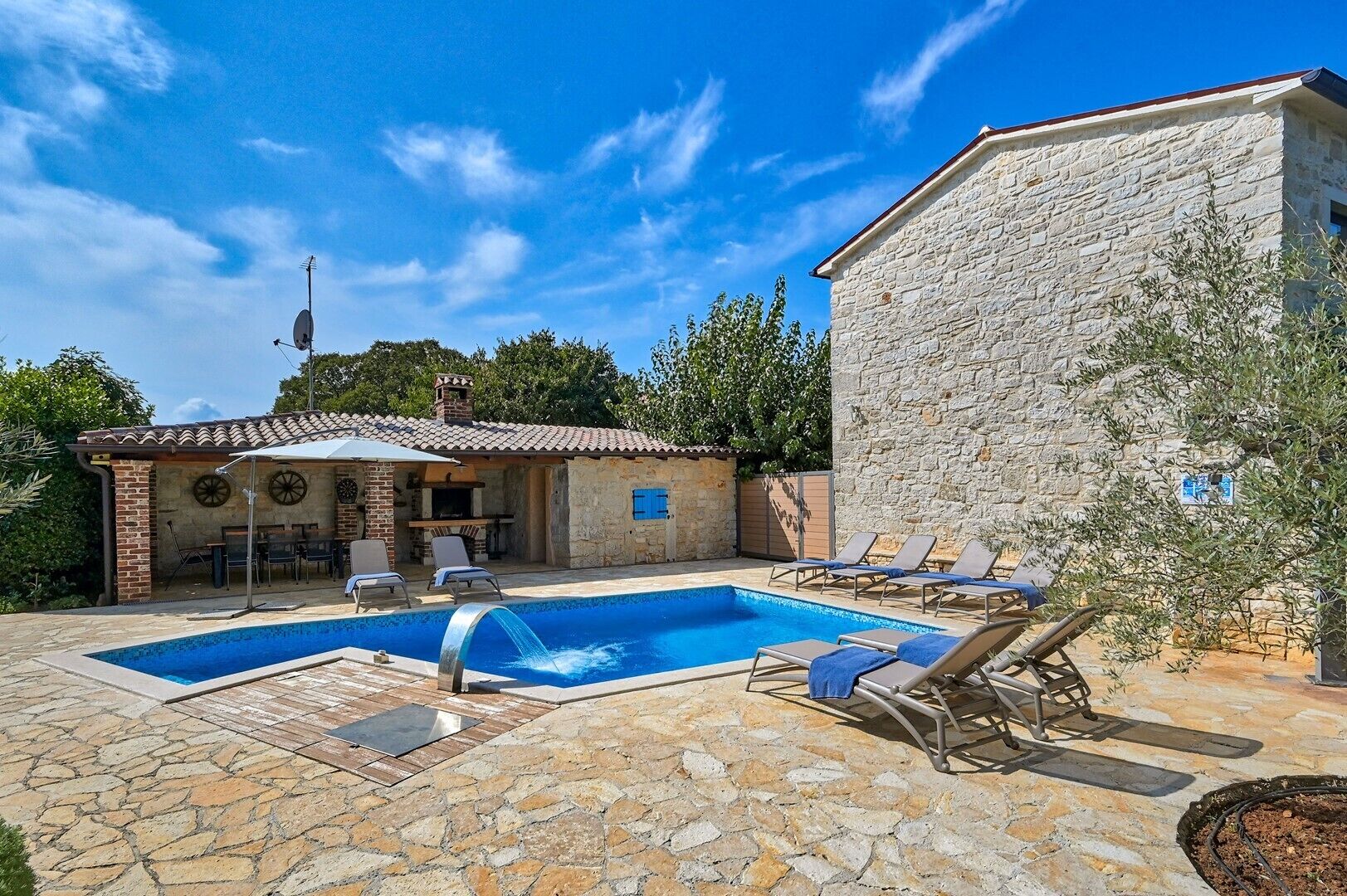 Ein Steinhaus mit Pool, Sitzgelegenheiten im Freien und einer Grillzone.