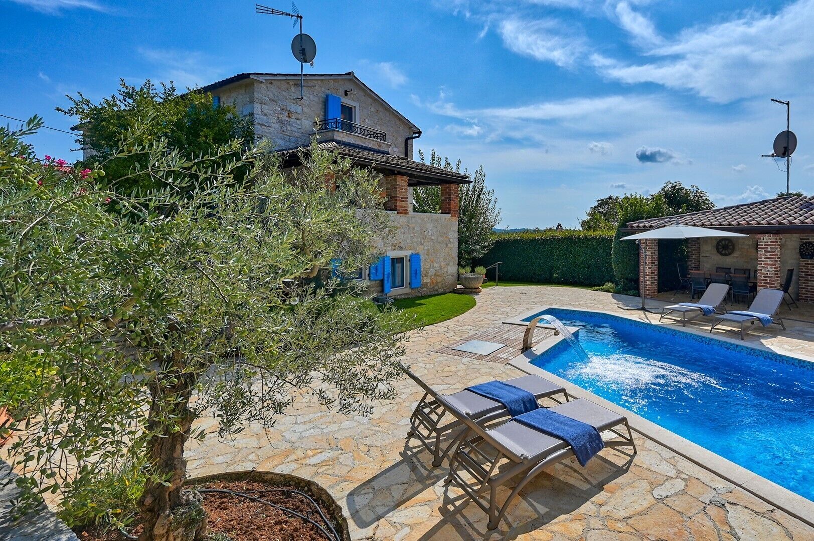 A stone pool with lounge chairs, a stone building with a balcony, and a tree in the foreground.