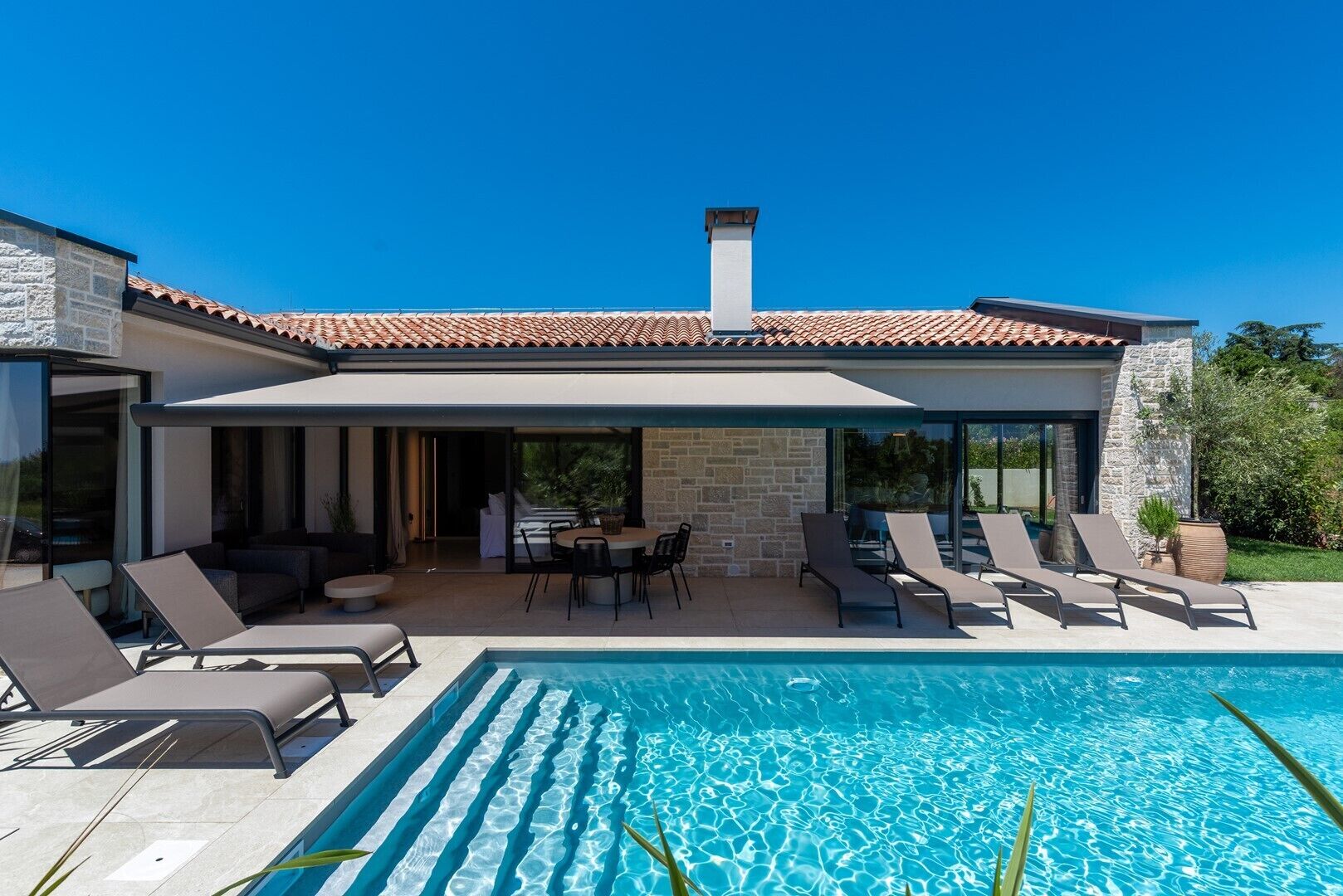 A modern house with a swimming pool, outdoor seating, and a stone facade.