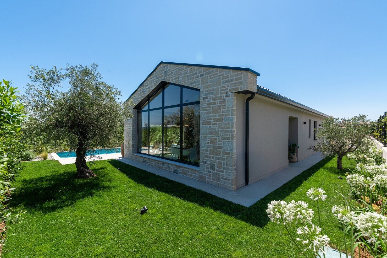 Una casa moderna con facciata in pietra, ampie finestre e un prato curato.