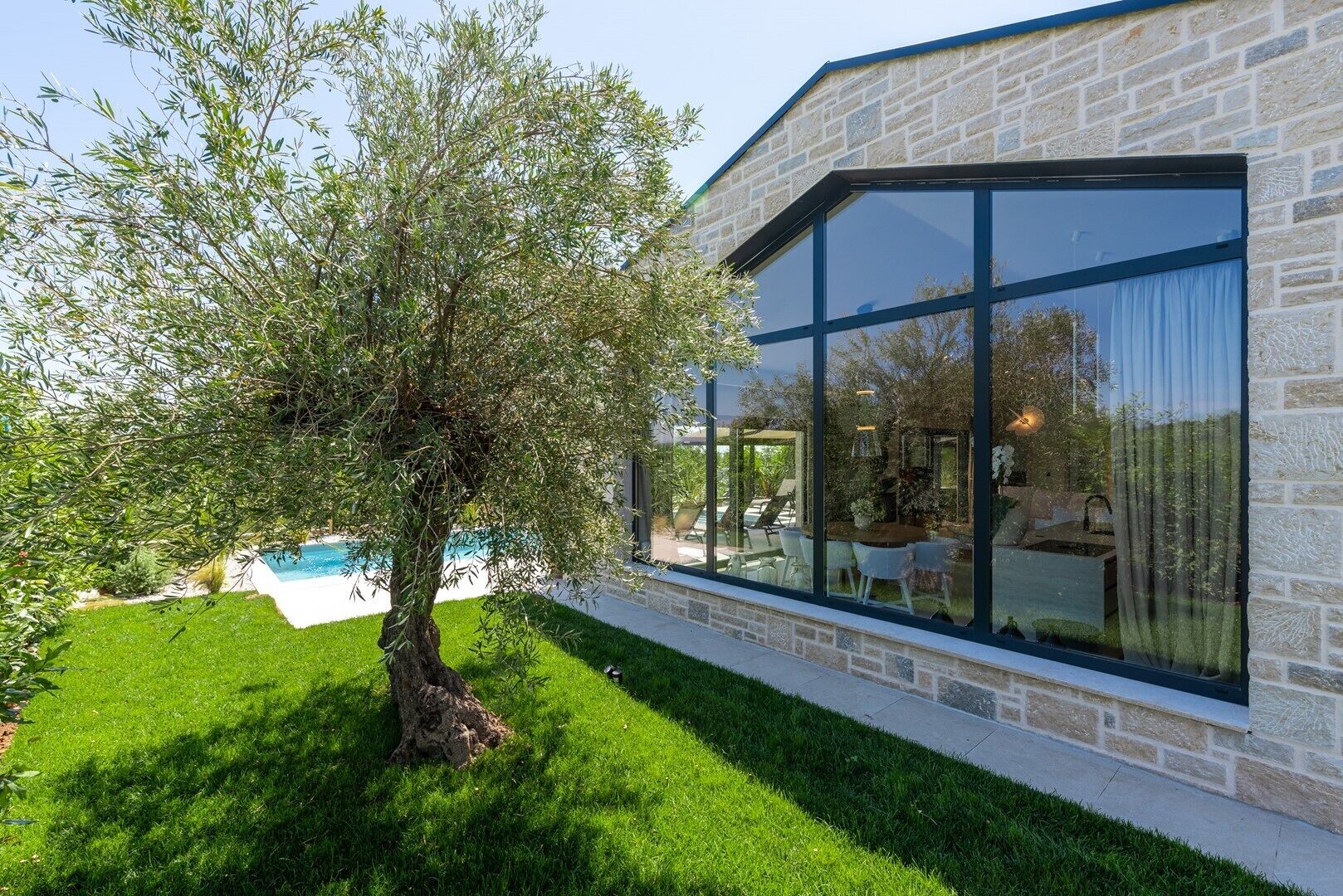 A modern house with a stone exterior, large windows, a swimming pool, and a well-maintained lawn.