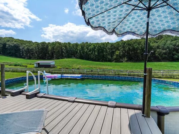 A swimming pool with a wooden deck, a small building, and a patterned umbrella.
