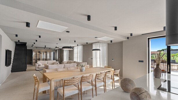 Un comedor moderno con una mesa y sillas de madera, un sofá y un gran ventanal con cortinas.