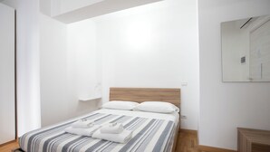 Un letto rifatto con lenzuola a righe, una testiera in legno e un comodino con una lampada.