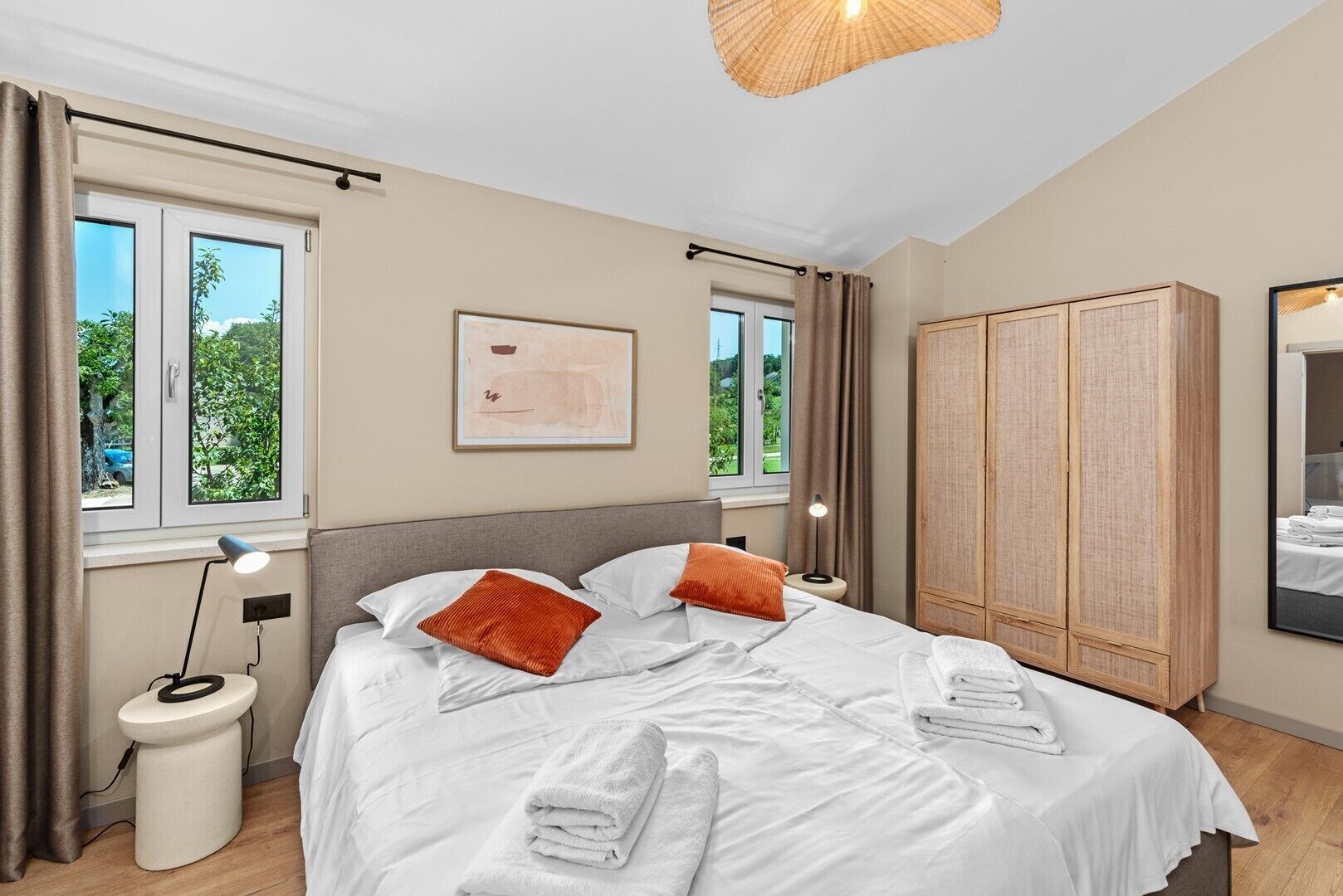 Une chambre à coucher avec un lit, des lampes de chevet, une armoire et une fenêtre donnant sur un paysage verdoyant.
