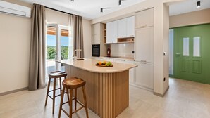 Eine moderne Küche mit Kochinsel, Barhocker und Blick auf Grünflächen.