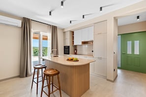 A modern kitchen with a central island, bar stools, and a view of greenery outside. - Beautiful Villa Vita for a holiday with private pool and BBQ for 6 guests (Beram)