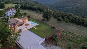 Ein modernes Haus mit Swimmingpool, umgeben von üppiger Vegetation und Hügeln.