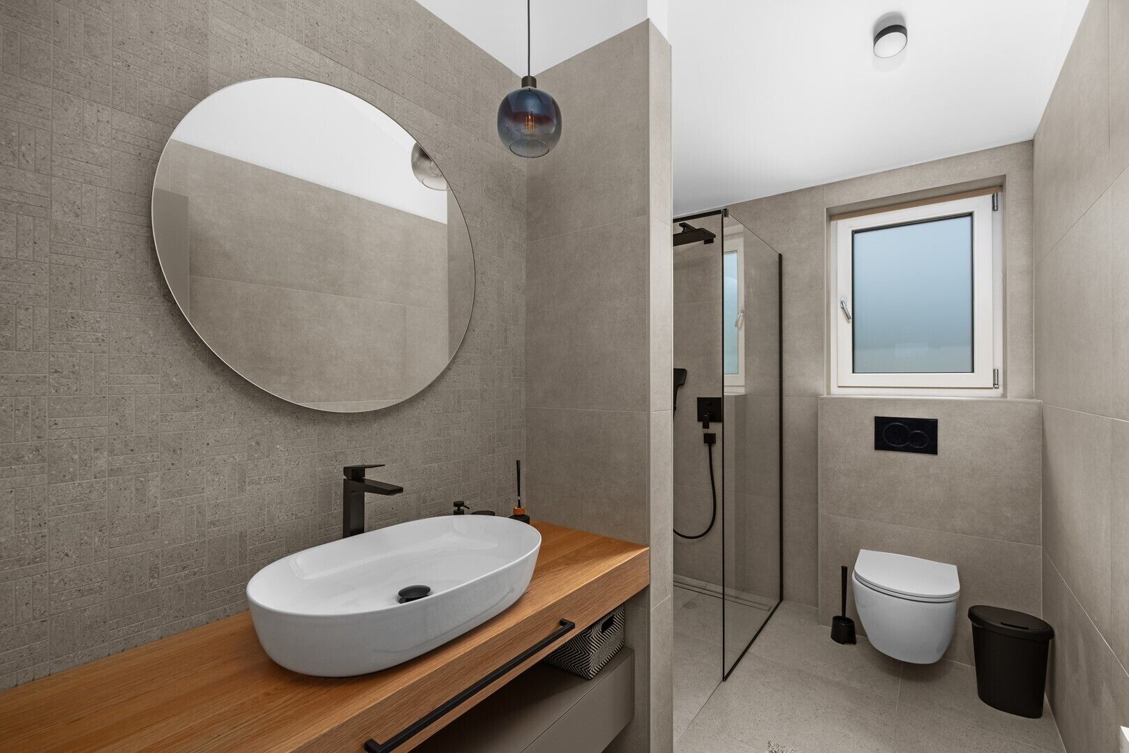 Une salle de bain moderne dotée d’un grand miroir rond, d’un lavabo sur pied, de toilettes et d’un espace douche.