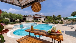 Area piscina con tavolo in legno, una ciotola di frutta e una bottiglia di bevanda.