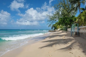 A beach with clear skies, calm waves, and a pathway leading to a gated area with greenery. - Luxury beachfront Villa with Chef, and staff (Fitts Village)