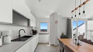 A modern kitchen with white cabinets, a black sink, and a coffee maker. There is a dining area with a wooden table and chairs, and a view of the outdoors through a large window. - Penthouse Stella Marini for 4+1 guests in Vabriga with Jacuzzi and sea view (Tar)