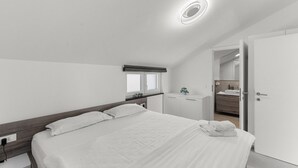 A modern bedroom with a large bed, a bedside table, a small desk, and a bathroom visible through an open door. - Penthouse Stella Marini for 4+1 guests in Vabriga with Jacuzzi and sea view (Tar)