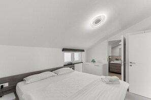 A modern bedroom with a large bed, a bedside table, a small desk, and a bathroom visible through an open door. - Penthouse Stella Marini for 4+1 guests in Vabriga with Jacuzzi and sea view (Tar)
