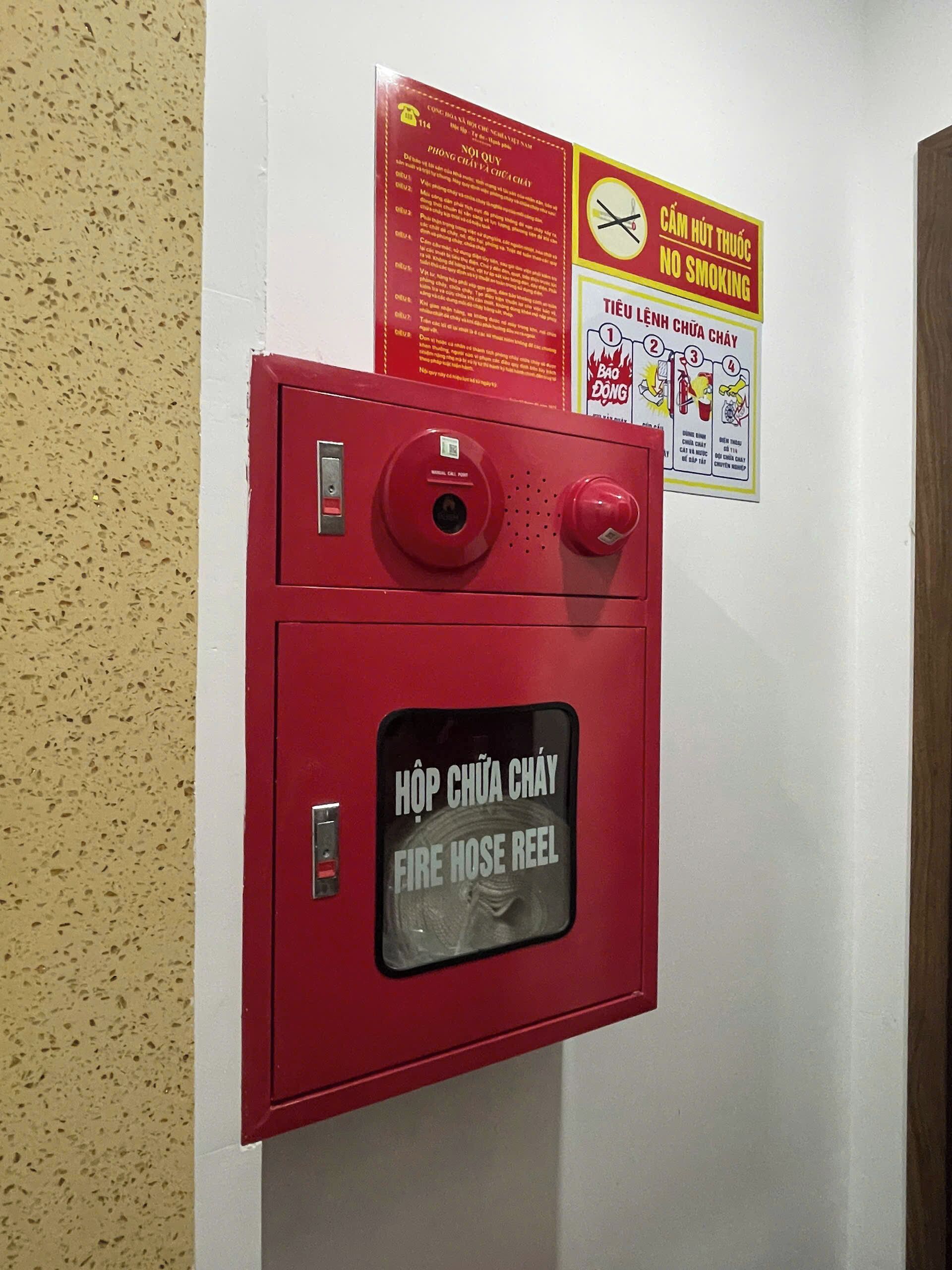 Ein an der Wand befestigter Feuerlöscher-Schlauchwagen mit Schildern, die 'Rauchen verboten' und 'Feuerlöscher-Schlauchwagen' auf Vietnamesisch anzeigen.